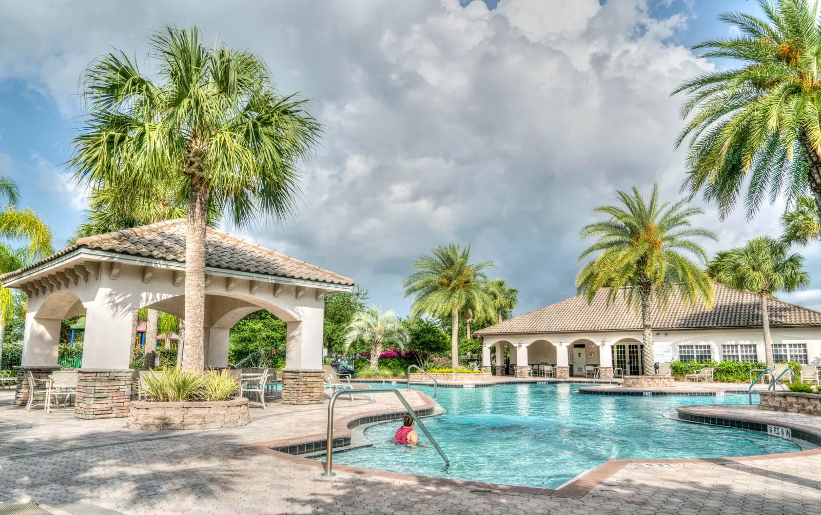 A community pool with palm trees, a gazebo and a clubhouse