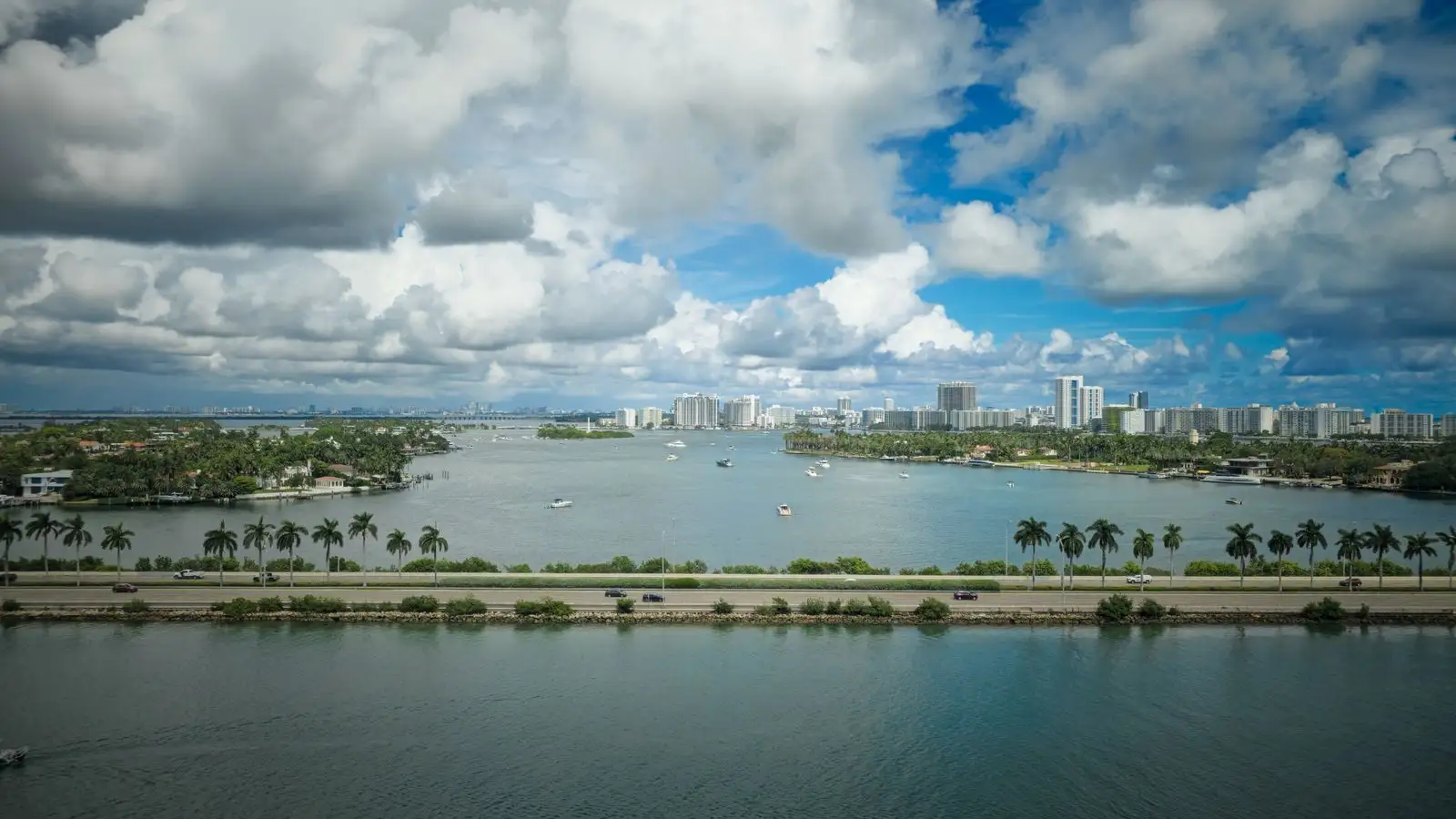 A palm-lined causeway across the bay in Miami, with high-rise condos on the far shore